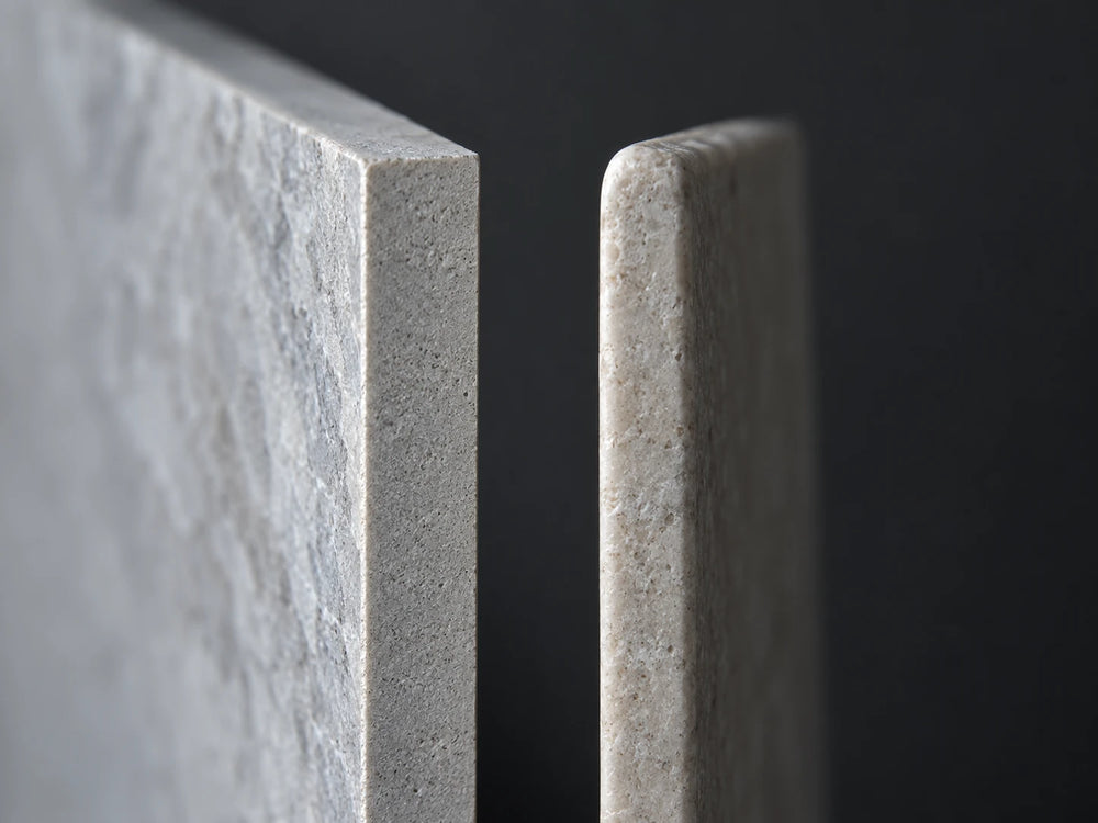 Two tile sample pieces photographed edge-on at eye level against a dark background: one edge is crisp and square, the other visibly softened and slightly rounded.