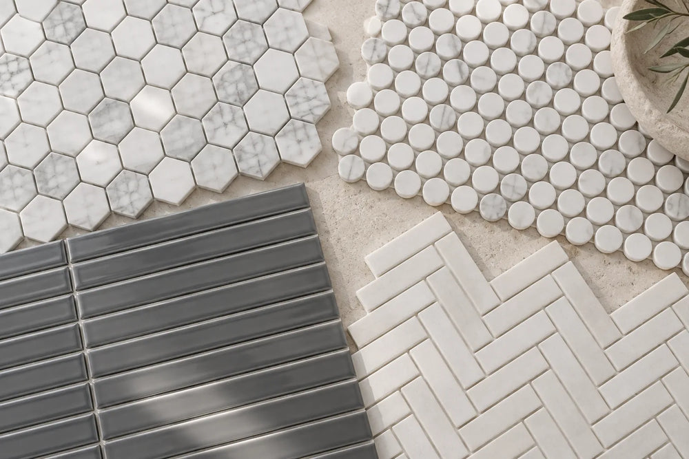 Four small-format tile sheets overlapping on a pale stone bench: white marble hexagons, white marble rounds, glossy graphite-grey strips and matt white herringbone.