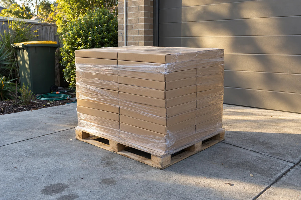 A pallet of flat tile cartons, wrapped in film, delivered on a suburban driveway beside the garage