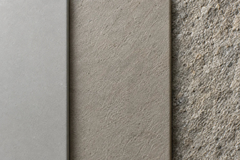 Close-up of three tile surfaces in low side light: smooth matt pale grey, lightly textured warm grey, and coarse and gritty.