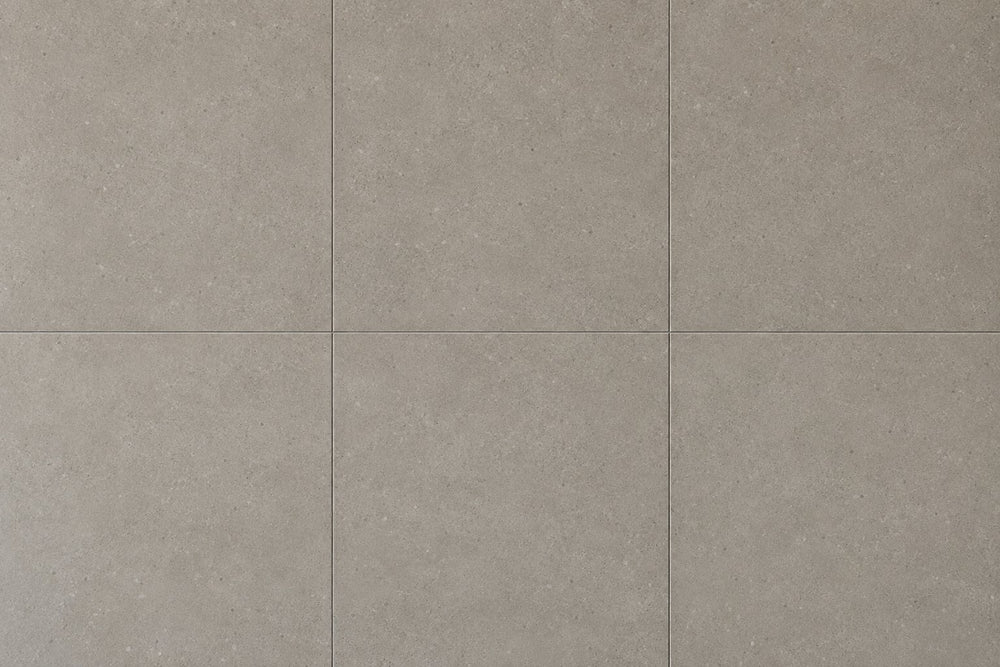 Editorial wall study: large square concrete-look tiles in a warm mid grey, laid in a grid with very fine joints, their flat powdery surface scattered with pale aggregate speckle under even daylight. Generated illustration, not a Tilekind product.
