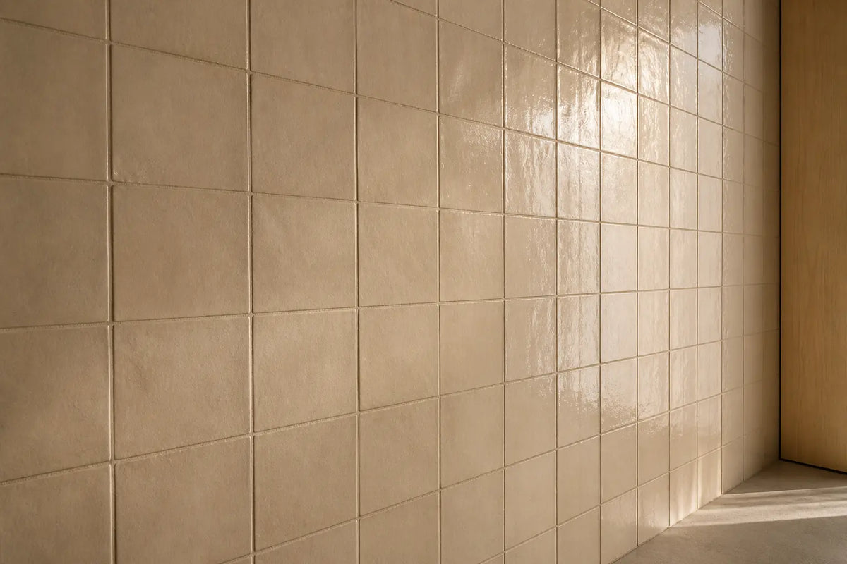 Plain tiled wall in low raking daylight, where one run of tiles returns a soft highlight and the run beside it stays flat and matt.