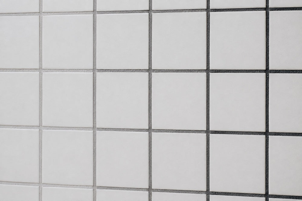 Editorial scene: plain white matt wall tiles with three adjacent runs of dried grout in light grey, mid grey and charcoal, showing how grout colour changes the same tile. Generated illustration, not a Tilekind product.