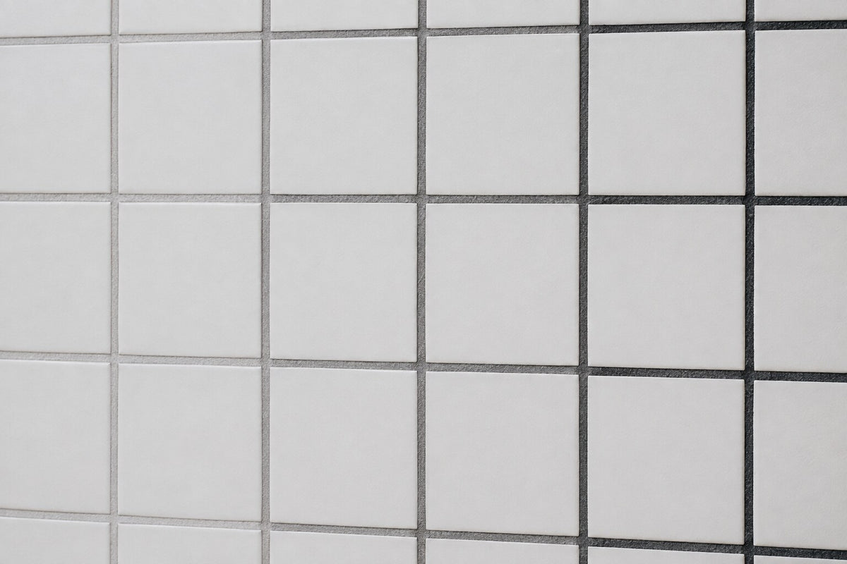 Editorial scene: plain white matt wall tiles with three adjacent runs of dried grout in light grey, mid grey and charcoal, showing how grout colour changes the same tile. Generated illustration, not a Tilekind product.