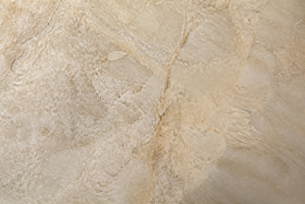 Close-up of a continuous pale stone surface with crystalline grain and warm veining under raking light