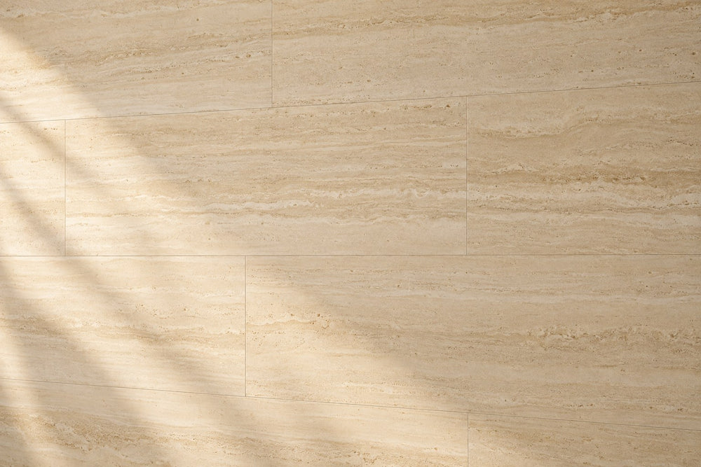 Editorial wall study: large ivory travertine-look tiles with a fine horizontal vein-cut grain, under soft late-afternoon daylight that throws a diagonal window shadow across the left. Quiet joints. Generated illustration, not a Tilekind product.