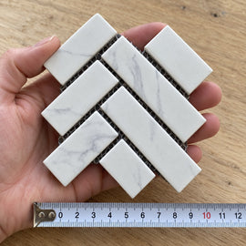 Carrara Herringbone Mosaic Tile sample held in a hand.