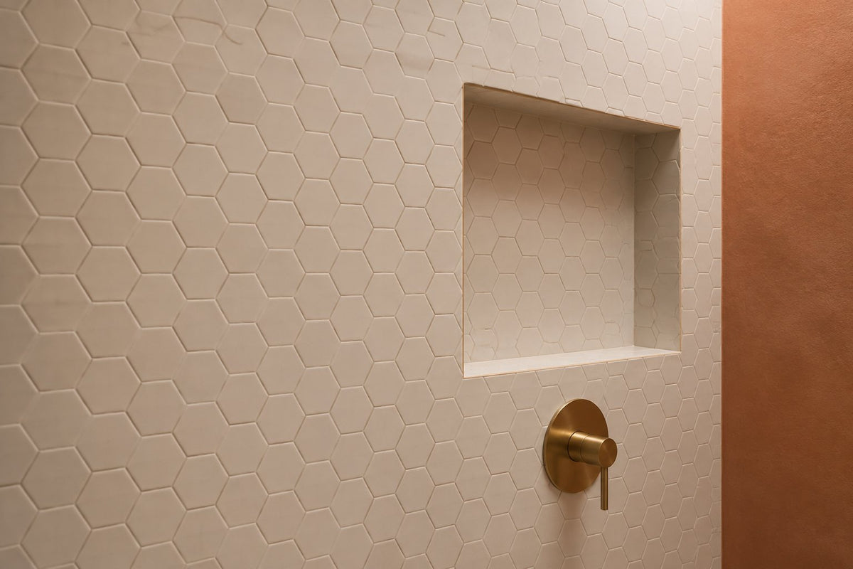 Small white hexagon mosaic on a bathroom wall and niche with soft grey grout and brushed brass tapware, warm evening light.