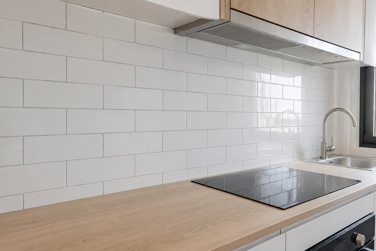 White gloss subway tiles laid in brick bond on a kitchen splashback above a pale timber bench, morning light.