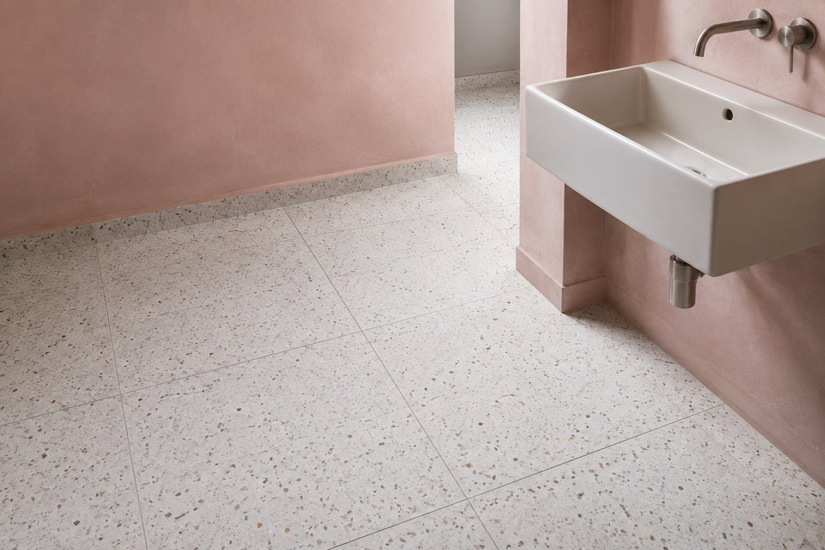 White terrazzo-look floor tiles with fine multicolour aggregate in a bathroom with blush plaster walls and a wall-hung basin.